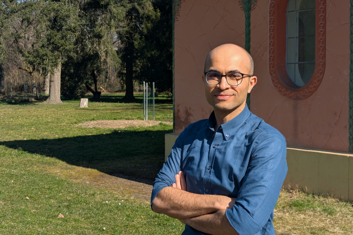 Photo of Navid Haghmoradi standing outside in a park near a building with trees in the background.
